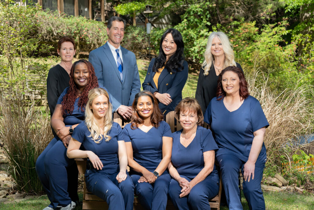 Dentistry With a Difference team poses outdoors, smiling in blue scrubs and business attire