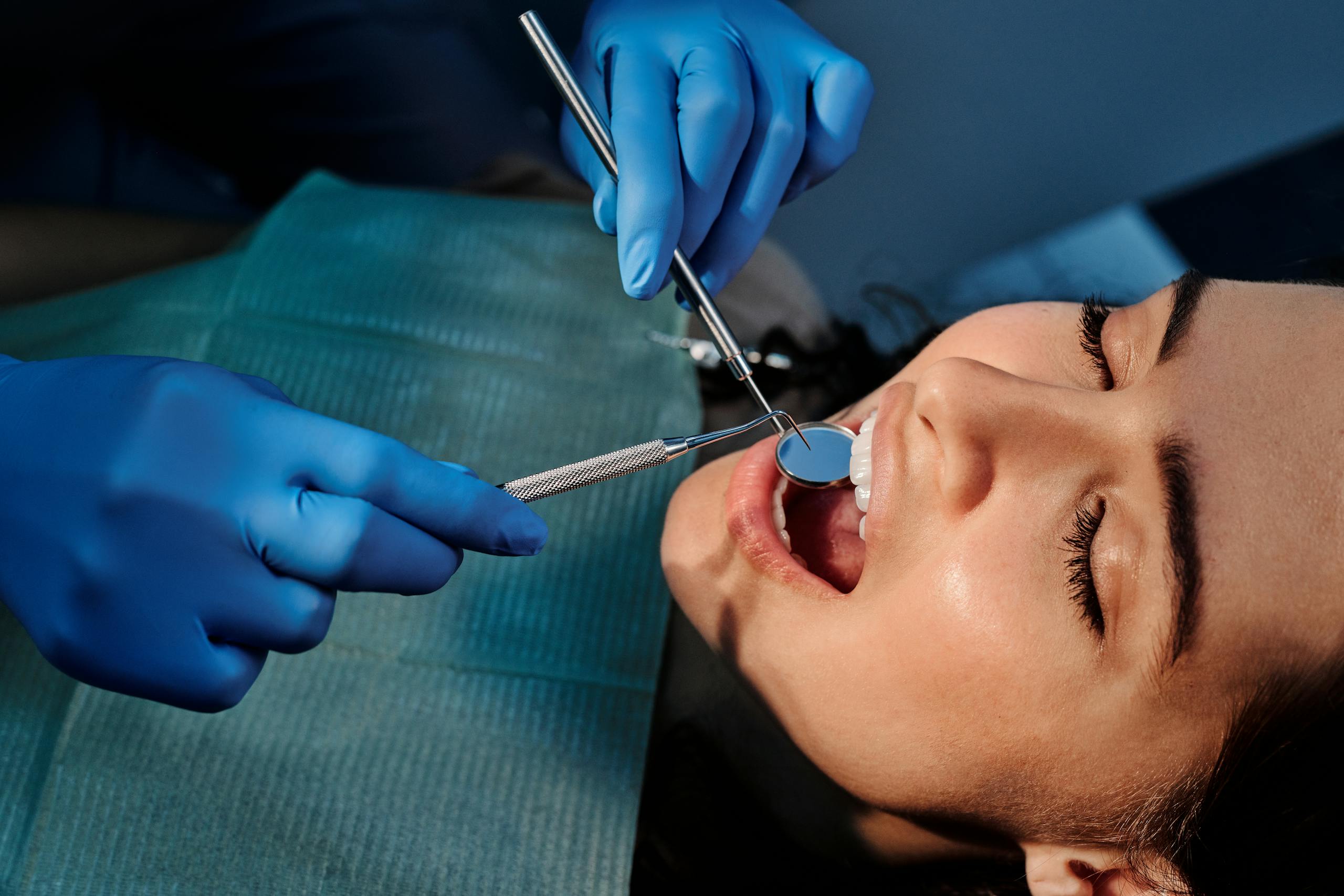 A patient receives a routine dental cleaning, with a dentist using a mirror and scaler 