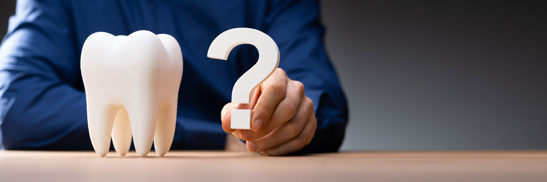 A person in a blue shirt holds a large question mark beside a model of a tooth, symbolizing dental questions 