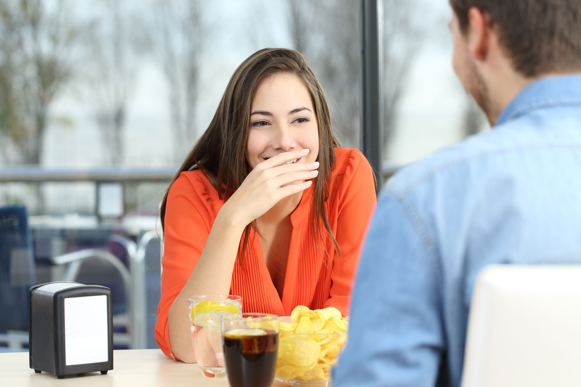 A woman sitting at a table, covering her smile with her hand, hinting at the confidence boost crown lengthening 