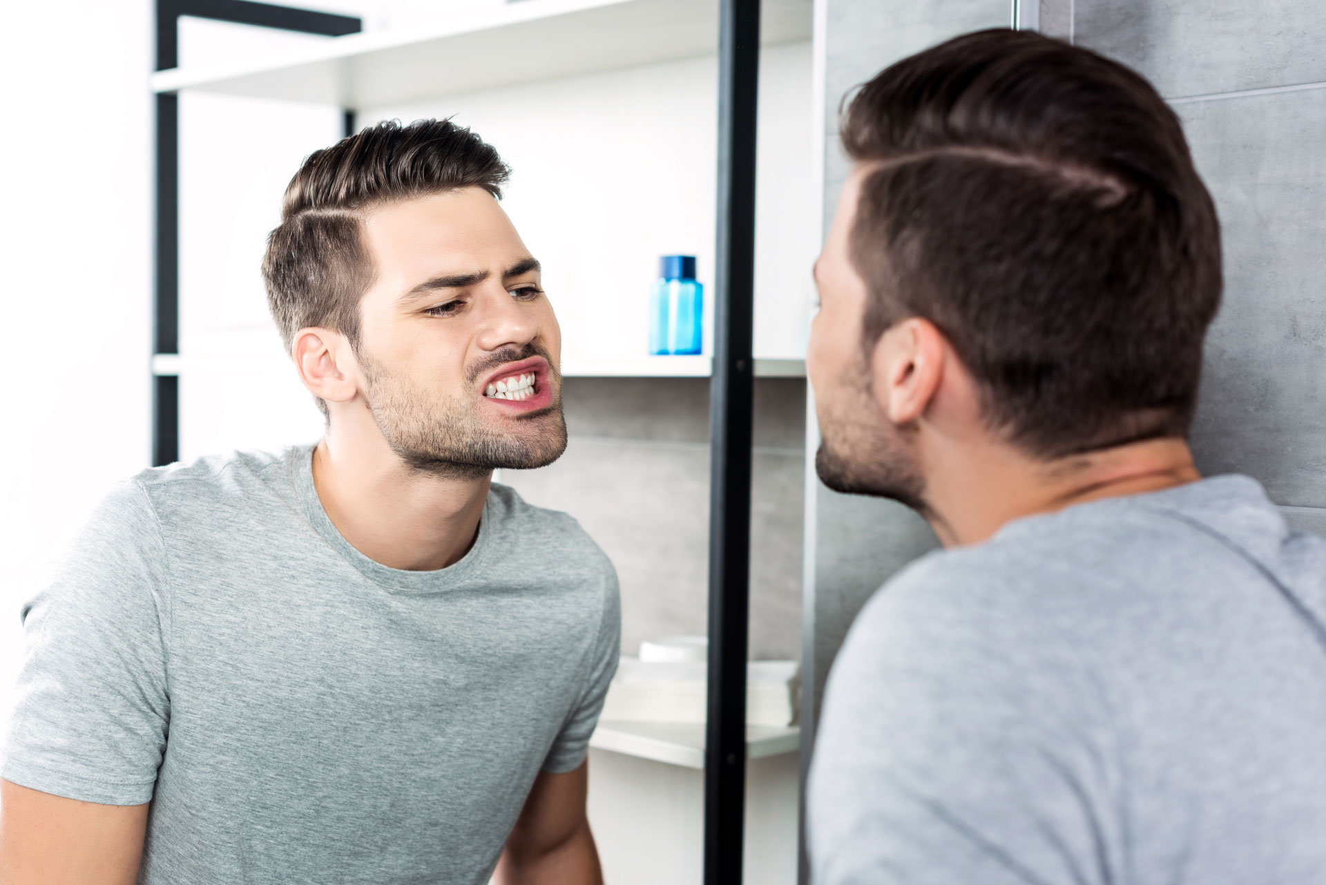 A man examining his gums in the mirror, focusing on their shape and symmetry, often improved through gum contouring