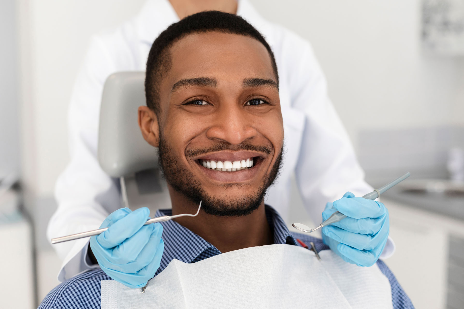 A smiling male patient in a dental chair, with a dentist holding dental tools during a general dentistry appointment