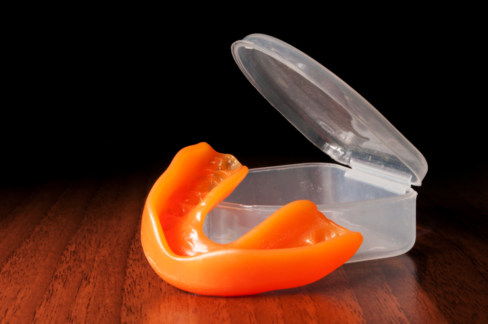 An orange sports mouthguard placed next to an open clear storage case on a wooden surface