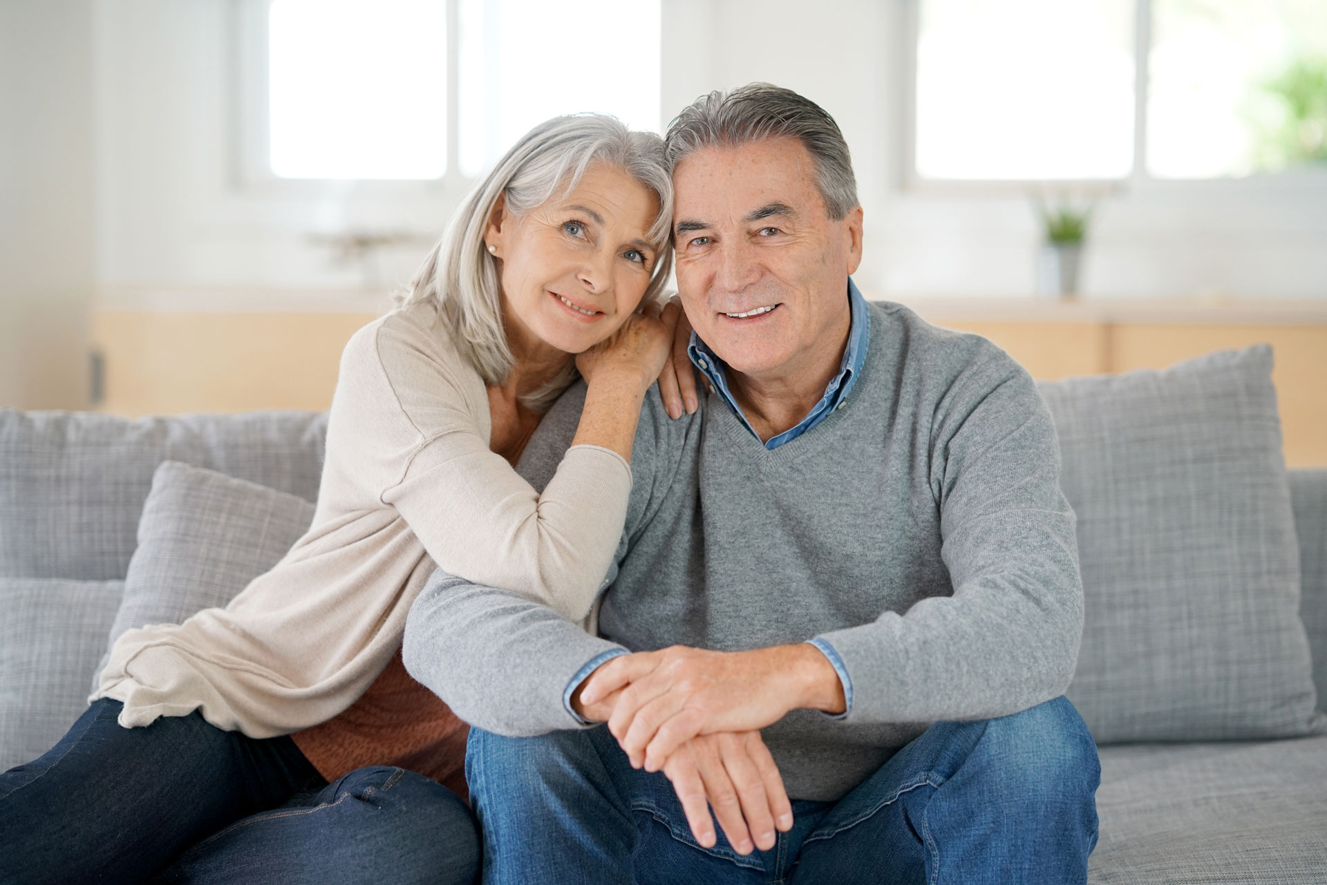 An older couple sitting closely on a couch, smiling warmly, showcasing the natural look achievable through dental bonding