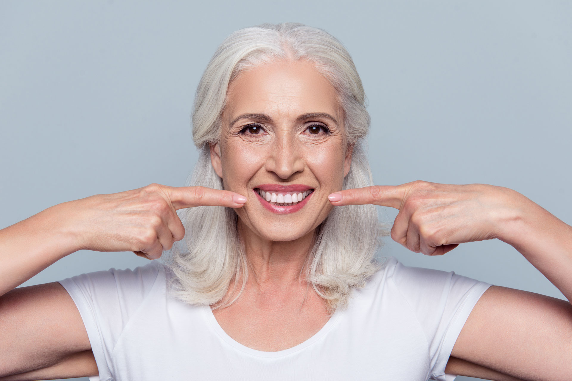 A smiling older woman pointing to her jawline and teeth, representing the potential benefits of Botox 