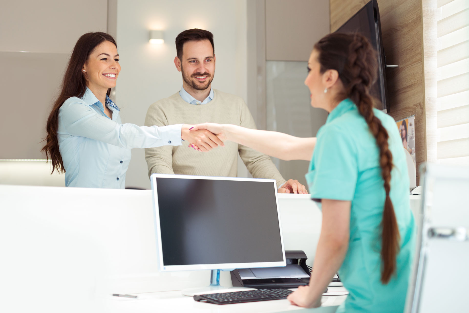 A smiling couple greets a dental receptionist in a Dentistry With a Difference office