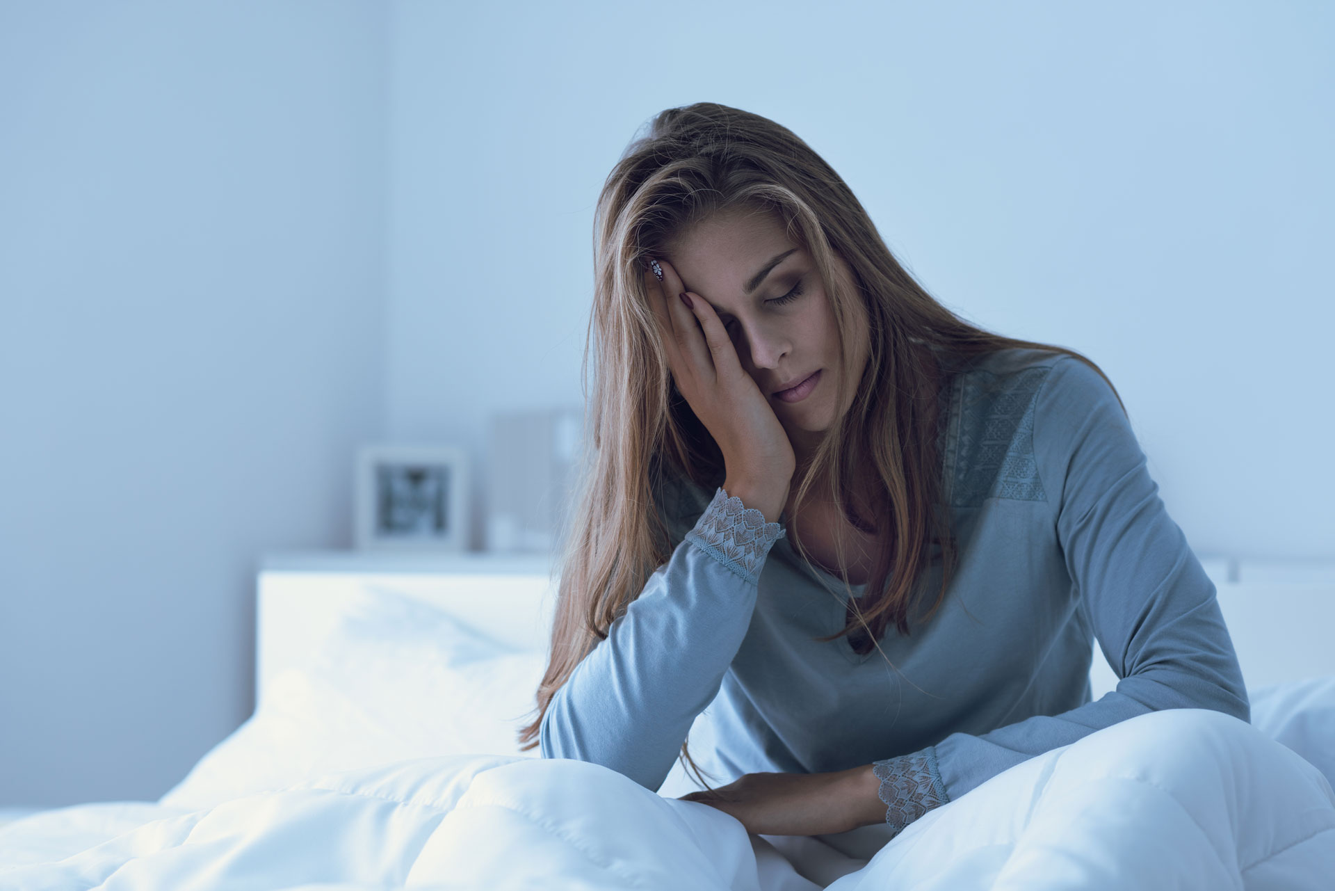 A tired woman sitting on her bed, representing the exhaustion caused by sleep apnea