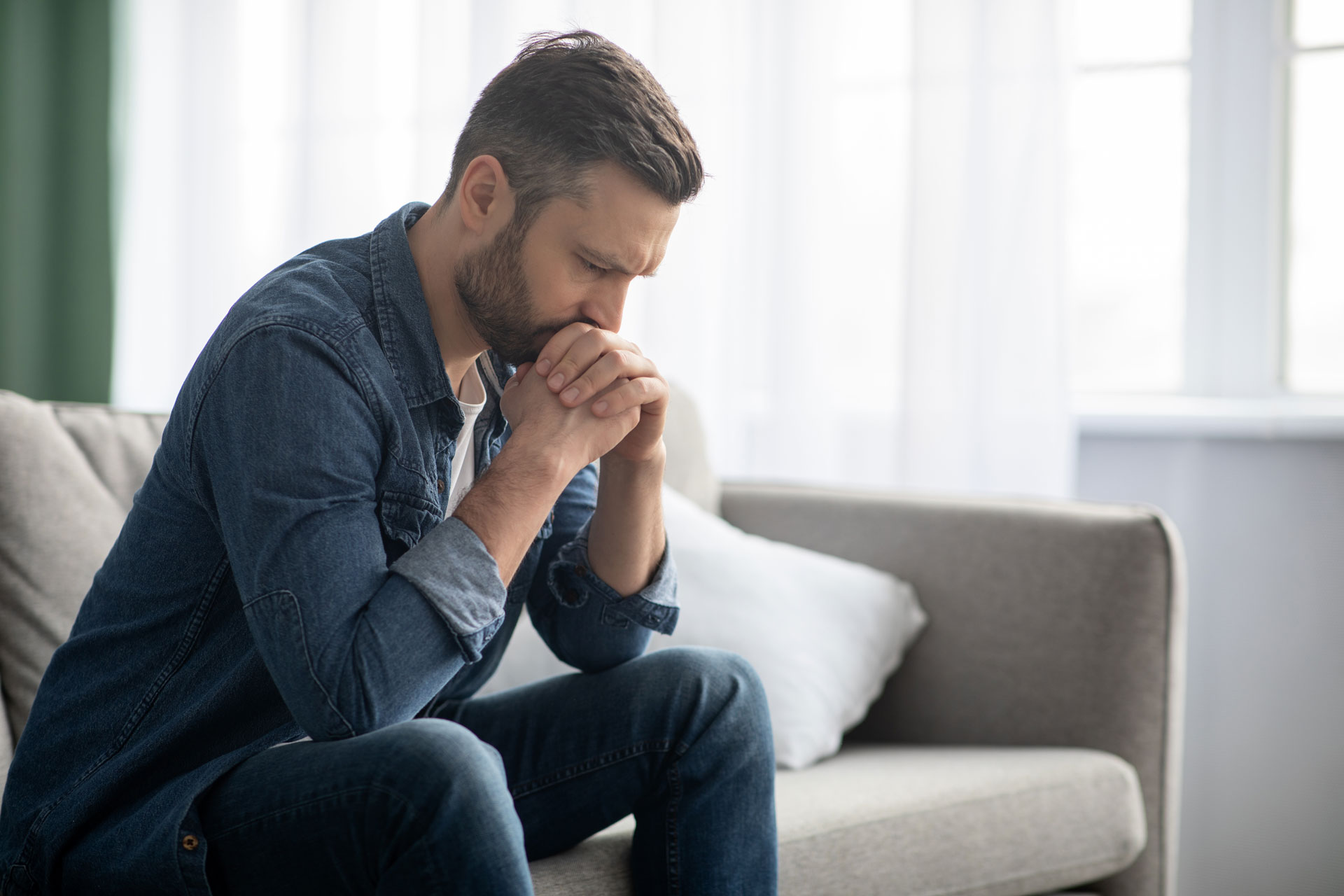 A man on a couch, looking anxious or contemplative, possibly thinking about having sedation dentistry