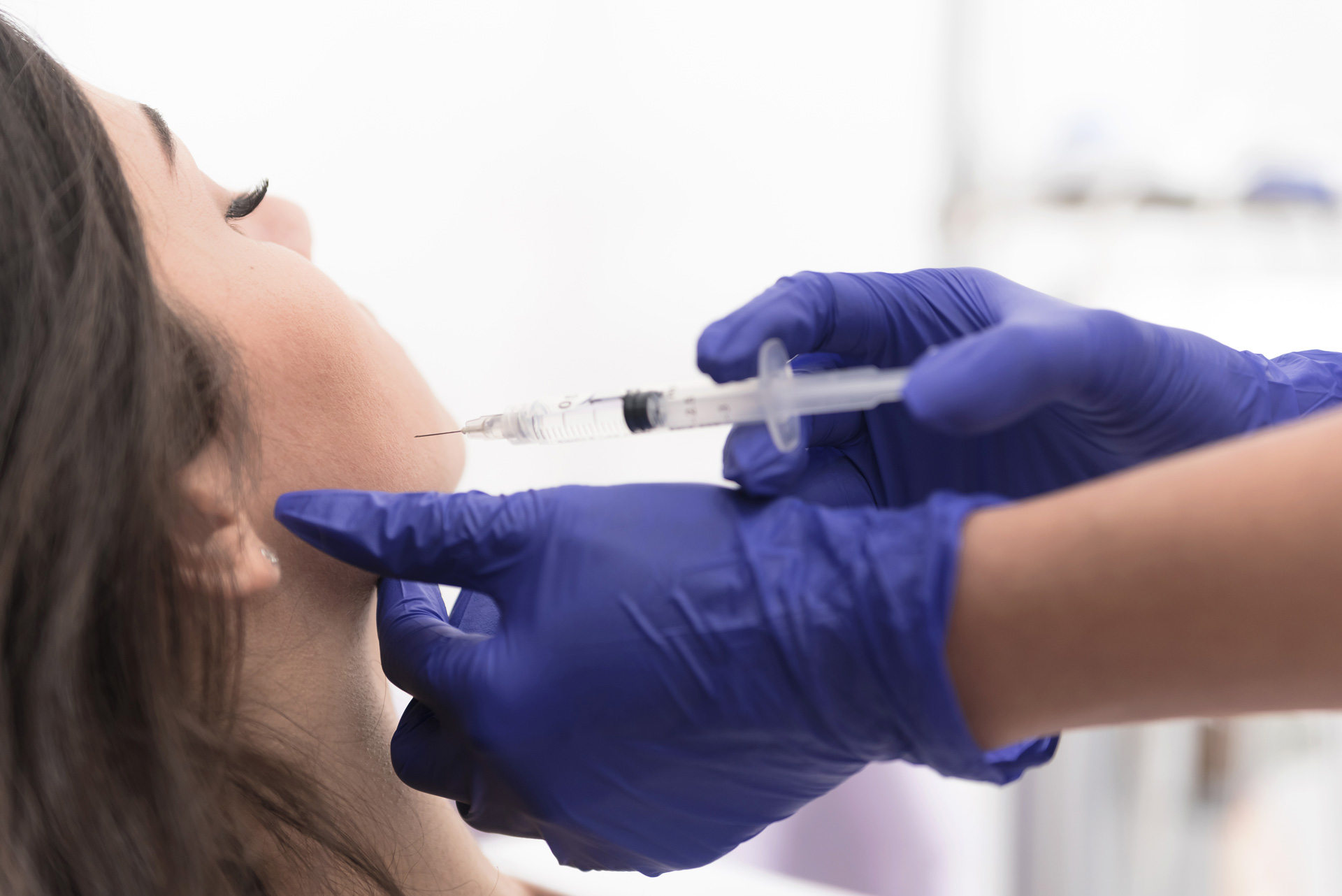 Close-up of a medical professional wearing blue gloves administering a Botox injection into a patient’s jaw area