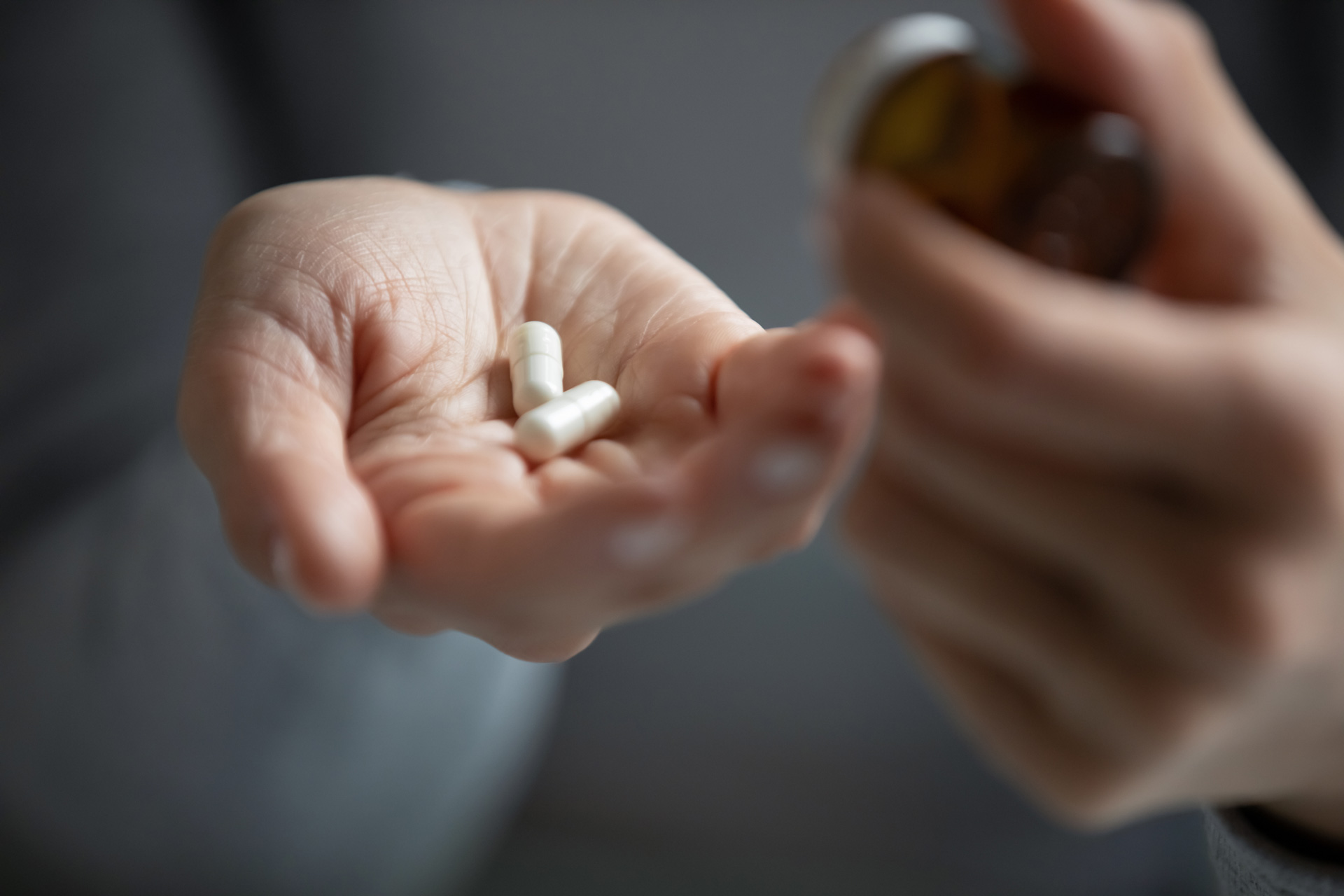 Close-up of a hand holding two white capsules, with another hand opening a brown pill bottle, representing oral sedation 